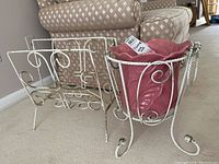 Front angled view of white metal plant stand with pink ceramic planter and matching metal magazine rack placed on beige carpet near a sofa.