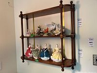 Front view of dark stained wood wall shelf with two shelves and decorative figurines on shelves (figurines not included).