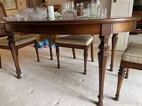 Side view of wood dining table with carved legs and items on top (not included).