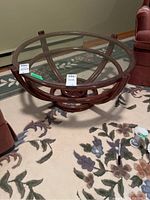 Full view of the round table showing the glass top and bentwood rattan base on a floral carpet.