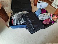Two suitcases opened showing assorted women's clothes, scarves, gloves, and a crossbody bag inside.