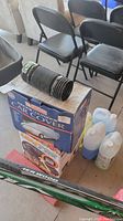 Overview photo showing the car cover box, leaf blower hose, safety kit box, and several bottles of window washing fluid positioned on the floor near folding chairs.