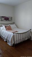 Full view of metal double bed frame assembled with white bedding, showing general condition of the frame and its structure.