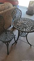 Photo of the metal round bistro table with ornate design and two matching chairs with detailed backs and seats.