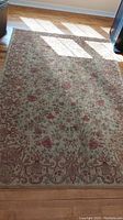 Carpet laid on wooden floor in daylight, showing full view with floral and scroll border pattern.