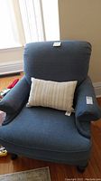Blue oversized recliner chair with curved armrests, high cushioned back, and a striped lumbar pillow on the seat, photographed from the front and top angles.