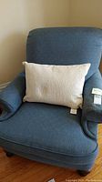 Front view of blue recliner chair with beige lumbar pillow on seat, showing cushioned back and arms, seat cushion, and wooden legs.