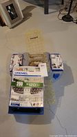 Photo showing closed plastic blue case containing Dremel accessory kit, visible labeling and contents inside clear cover.