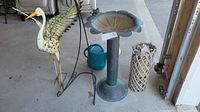 Wide view of all items in the lot arranged on concrete floor including metal bird, birdbath, watering can, basket, and lantern
