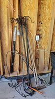 Overview of multiple metal shepherd hooks and garden stakes leaning against wooden wall.