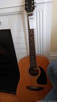 Full length photo of the Epi acoustic guitar showing the body, neck, and headstock against a white wall background.