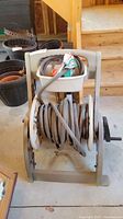 Front view of the grey garden hose coiled on a plastic reel with black wheels and crank handle, with accessories in an upper tray.