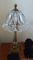 Full view of one solid brass table lamp with glass shade on wooden surface against plain wall