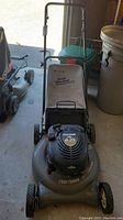 Front angle of the mower showing handle, deck, wheels, and grass collection bag