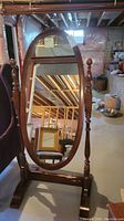 Full view of the oval wooden framed floor mirror with stand and turned wood posts on sides. Visible wear and damage at the bottom of the stand base.