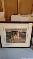 Two framed prints showing identical artwork of a church with steeple in a natural setting, leaning against basement wall.