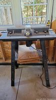 Full view of the Black & Decker router table with metal stand, showing the router mounted underneath and a window background.
