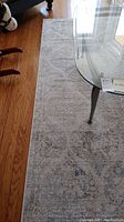 Photo showing side view of the grey and white patterned rug, displaying detailed pattern and placement next to hardwood floor and glass table.