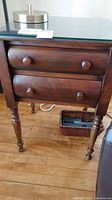 Front of wooden side table showing two drawers with round wooden knobs and turned legs.