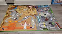 Wide view of Hot Wheels play mat on floor showing city and desert racing track design with small toy cars placed on it.