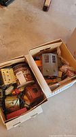 Two cardboard boxes with assorted vintage train set items and accessories