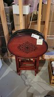 Set of four wooden TV trays nested in their storage stand, showing the oval tray tops with black decorative pattern and reddish-brown finish.