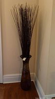 Full view of the tall floor vase with decorative sticks showing entire height and shape.