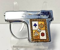 Side view of the chrome gun-shaped lighter with enamel panel showing club, crown, ship, and die design
