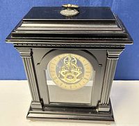 Front view of the black mantle clock with gold dial and decorative top key.
