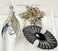 Two silver brooches displayed together, showing both designs and contrasting elements.