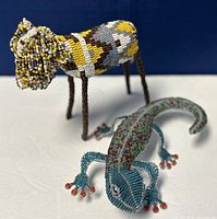 Side view showing both the beaded sheep standing on four wire legs and the lizard with detailed beadwork on its body and red-accented feet.