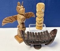 Front angle of three wood carvings including eagle totem, smaller figure, and xylophone on blue background.