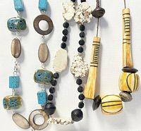 Close-up of three vintage beaded necklaces displayed side by side, showing varied bead materials and shapes including turquoise cubes, wooden rings, black lava stone spheres, and cream irregular stones.
