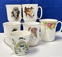 Photo showing six mugs including four dog-themed bone china mugs, one floral Royal Albert mug, and one F/F Turi Design mug with a man graphic.