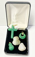 Five natural jade pendants displayed in a black and white jewelry box showing cross, Buddha figures, donut and double-gourd shapes.