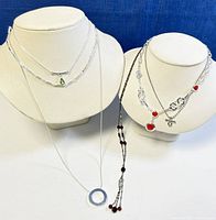 Six vintage Continental costume necklaces displayed on two white bust forms, various chain and pendant designs.