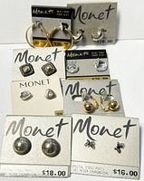 Full view of eight pairs of Monet costume earrings displayed on branded cards, showing variety of styles and materials.