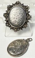 Front view of floral brooch and etched locket pendant side by side