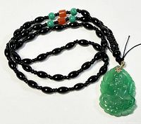 Full view of the 25 inch necklace showing black beads with turquoise and orange accents and a green carved jade Buddha pendant attached.