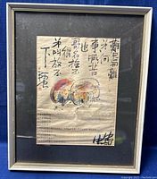 Full view of framed artwork showing Chinese calligraphy and two figures carrying large round objects on their backs.