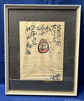 Front view of the framed artwork showing calligraphy and Daruma doll illustration with visible frame edges and black matting.