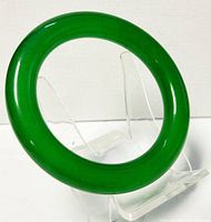 Close-up of the polished green jade bangle bracelet on a clear display stand.