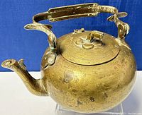 Old brass teapot front angle showing the round body, lid with broken hinge, and patina with dents.