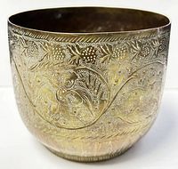 Angled front view of the brass planter pot showing detailed etched floral and fruit designs on the exterior.