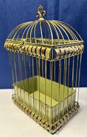 Full view of old metal birdcage showing gold and green distressed paint, decorative top finial, and rectangular shape with domed top.