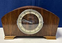 Front view of the old Solar German wooden mantle clock with Lotus brand on the dial, showing clock face, metallic rimmed glass cover, and base with metallic feet.