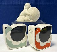 Front view of the Orla Kiely salt and pepper shakers with retro bird design in green and orange, alongside the beige stone sculpture in background.