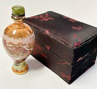 Hand painted glass perfume bottle standing next to a black fabric box with red embroidery.