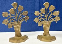 Pair of brass tulip bookends with flower bouquet design on blue fabric background, front view.