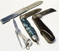 Four vintage pocket knives and cutters, laid on white surface showing wear and patina on blades and handles.